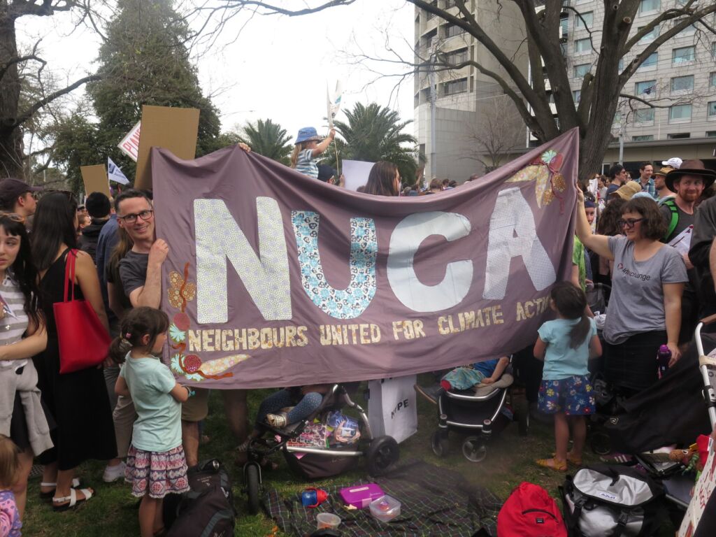 A group of people including kids holding a banner with the word NUCA stitched into it