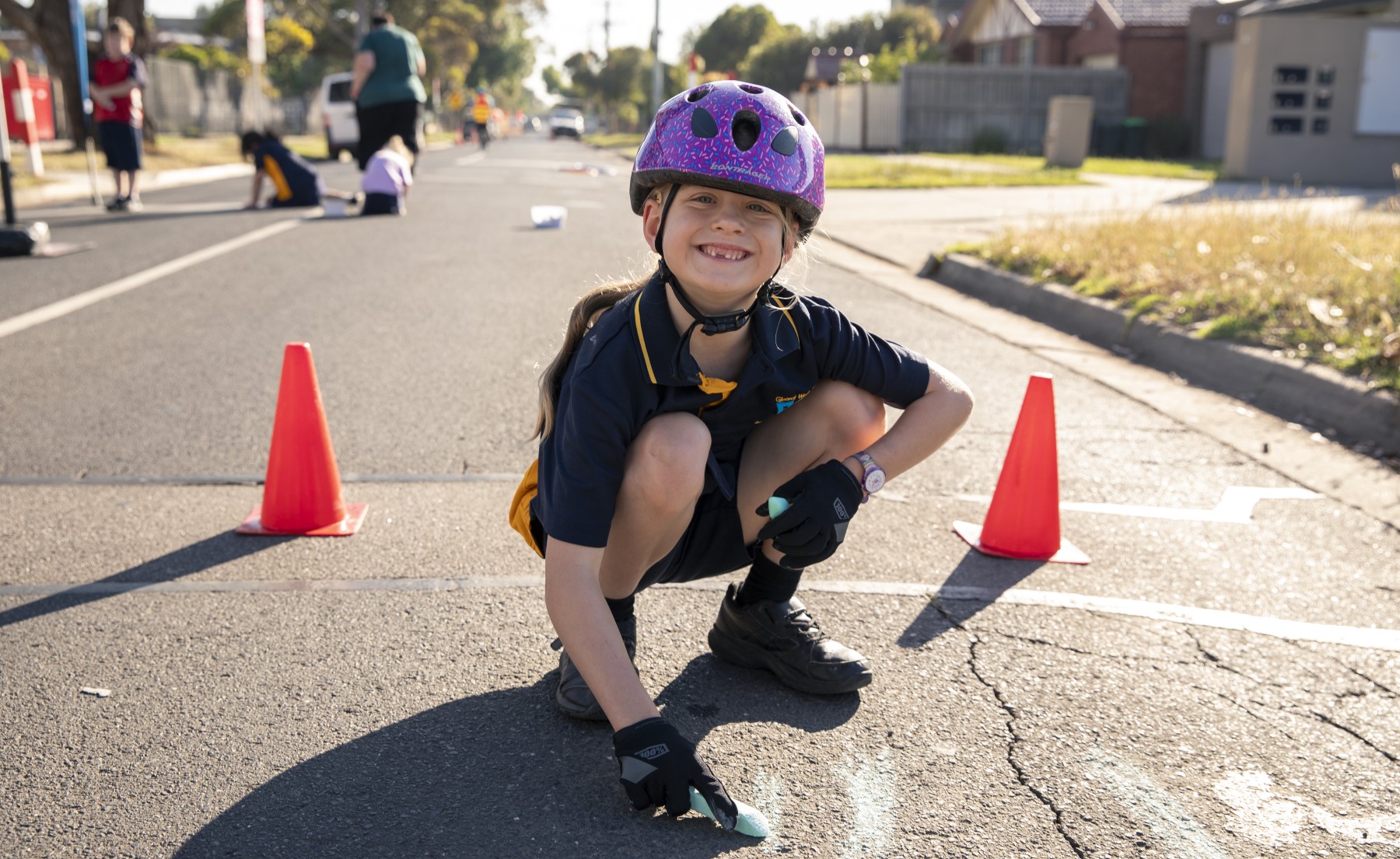 Young girl with bike helmet kneeling on a closed road drawing with chalk.
