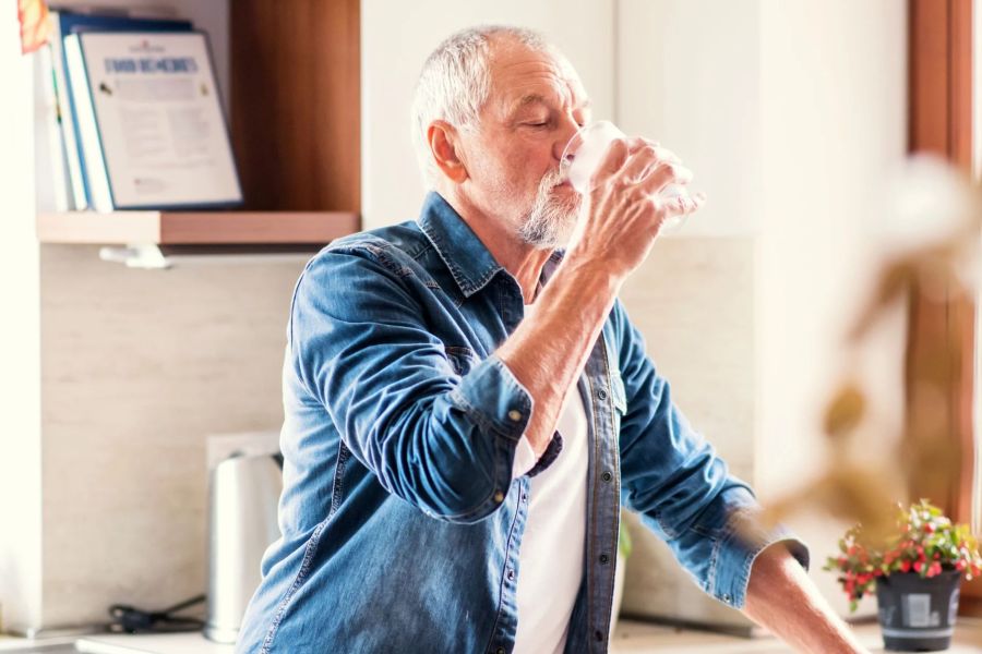 Older man in a kitchen drinking water.