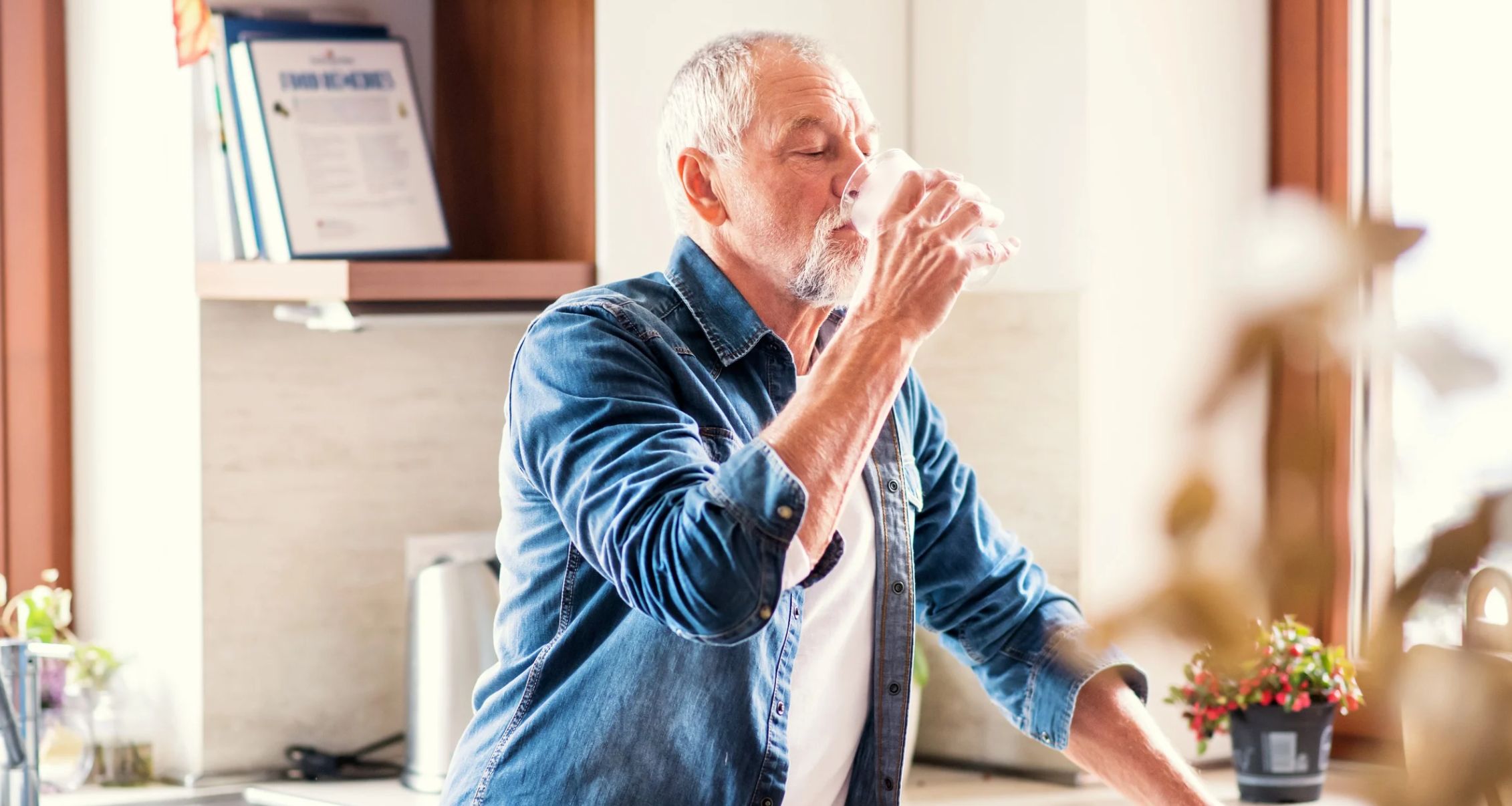 Older man in a kitchen drinking water.