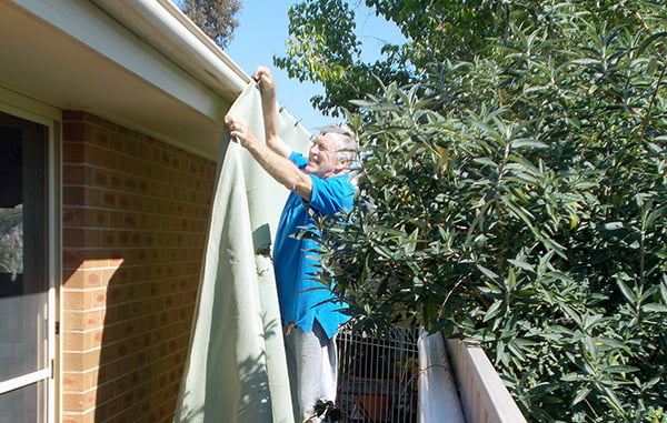 Person placing shade cloth on side of house