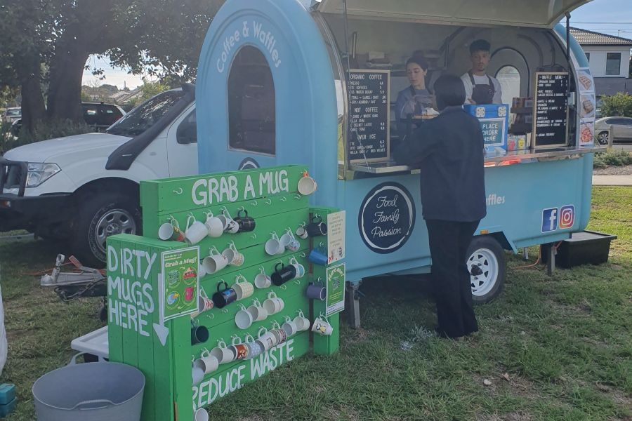 Person ordering coffee from coffee van with a board of reusable mugs
