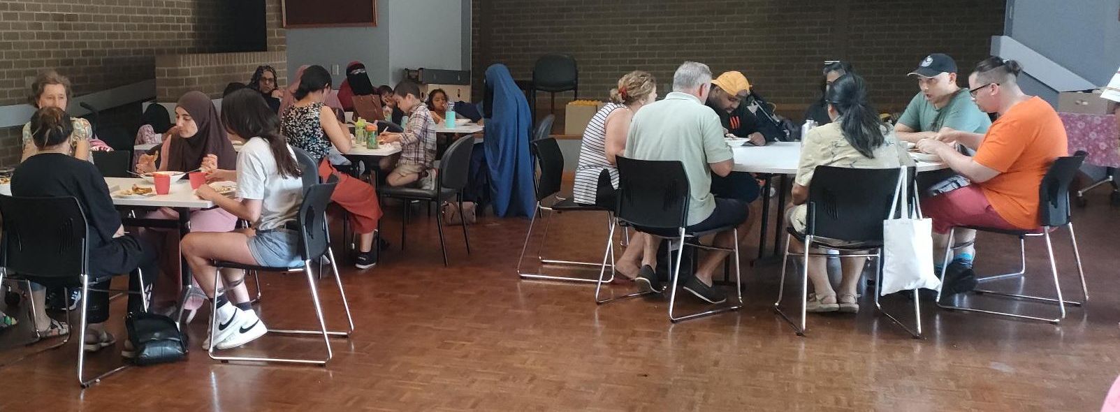 Groups of people sitting around table sin a hall eating lunch