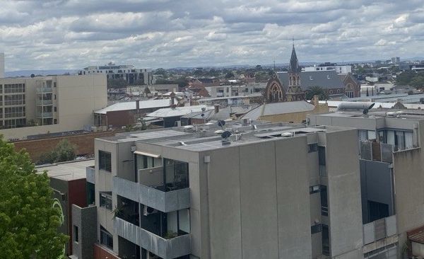 Photo of inner city suburb skyline with an apartment block with solar panels on roof in foreground.