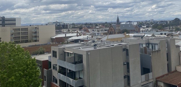 Photo of inner city suburb skyline with an apartment block with solar panels on roof in foreground.