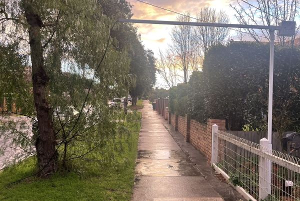 Photo of suburban street and foot path with an extended pole from a house going across the footpath.