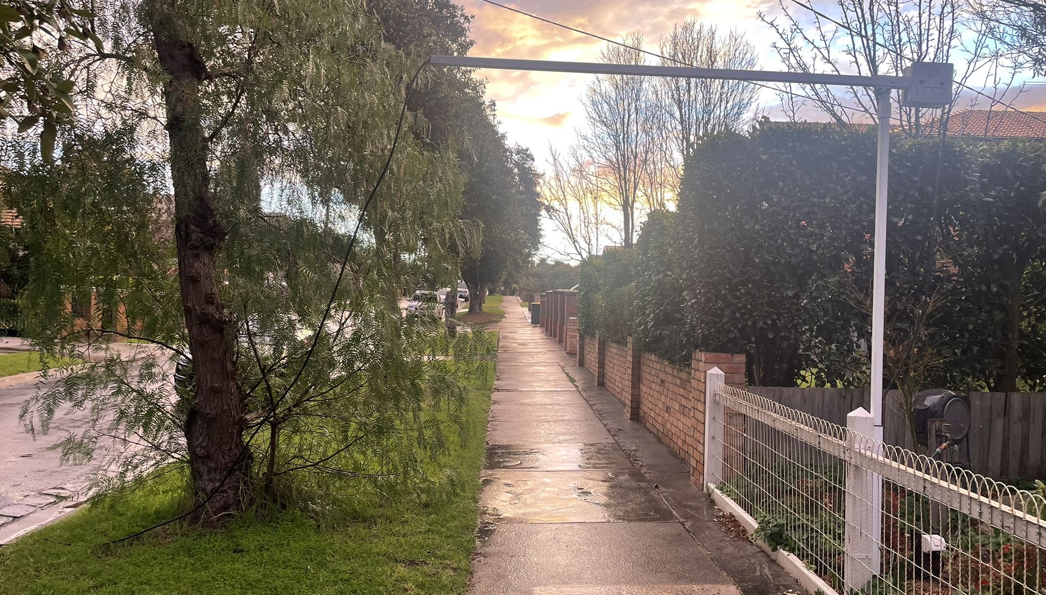 Photo of suburban street and foot path with an extended pole from a house going across the footpath.