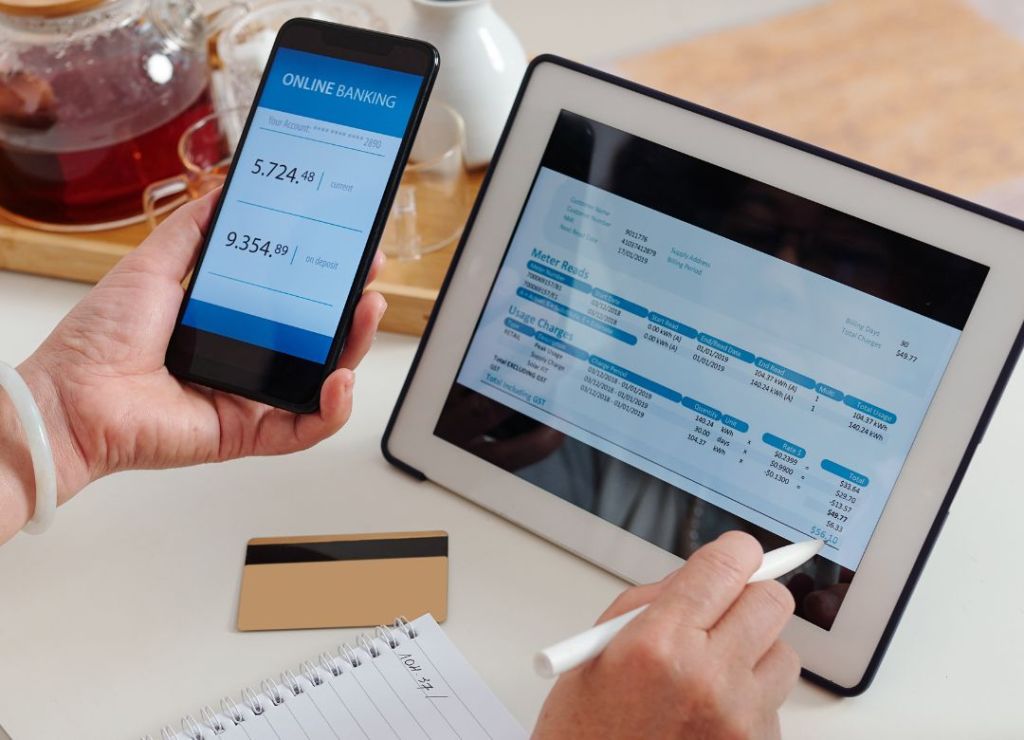 Image of person holding a mobile phone and an ipad on a table paying a power bill.