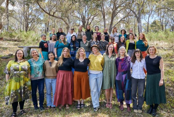 Group of women standing in three rows smiling at camera in a bush setting.