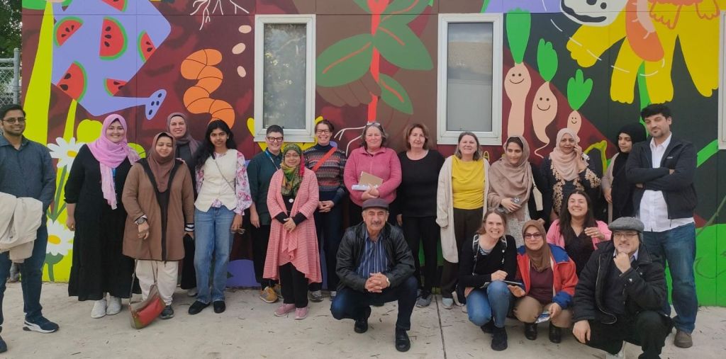 Group of 20 people standing in front of a colourful mural