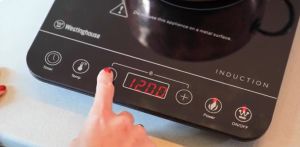 A hand pushing a button on a portable induction cooktop sitting on a bench.