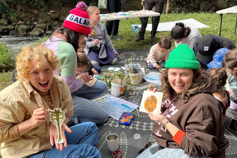 People sitting on a rug near a creek making artworks.