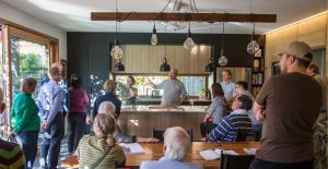 People standing around a kitchen with someone talking and pointing.