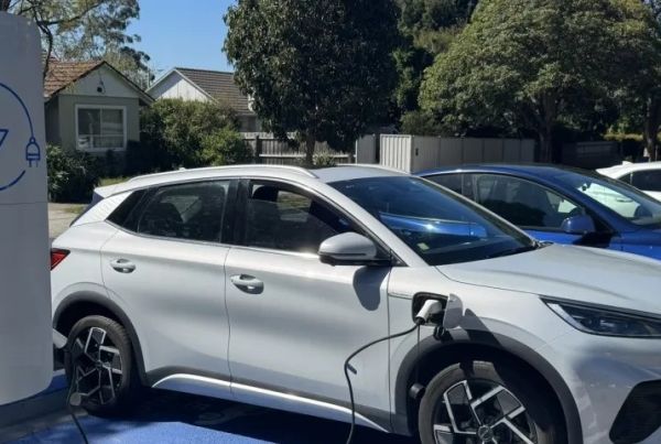 Electric cars parked on side of road with a car being charged with a charger on a streetlight pole.
