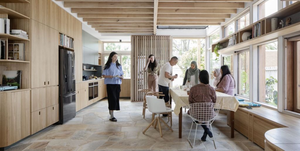 Inside of a light-filled home with family members gathering around a kitchen table