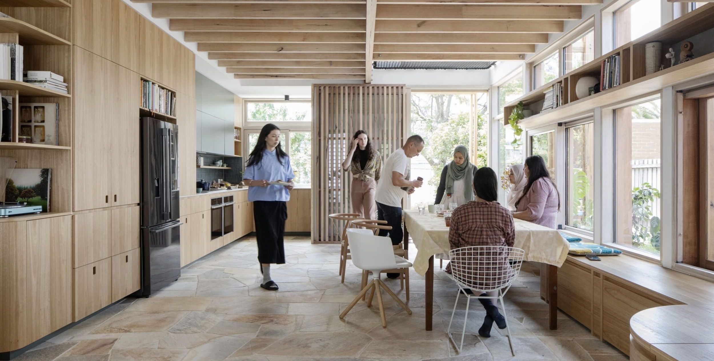Inside of a light-filled home with family members gathering around a kitchen table