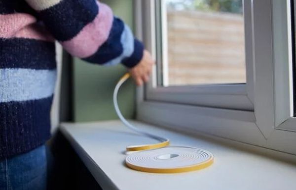 Photo of person placing draught-proofing tape to window frame