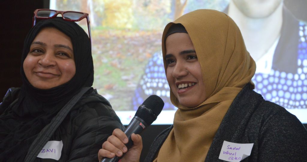 Two women smiling and speaking with one holding a microphone