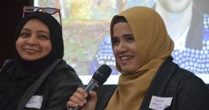 Two women smiling and speaking with one holding a microphone