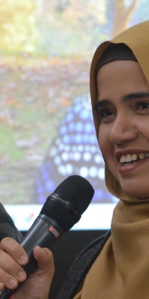 Two women smiling and speaking with one holding a microphone