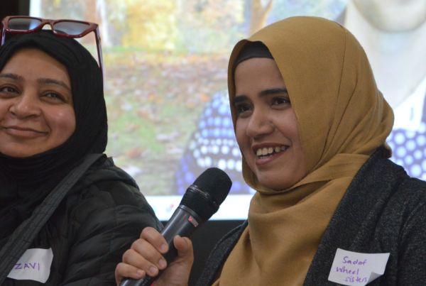 Two women smiling and speaking with one holding a microphone