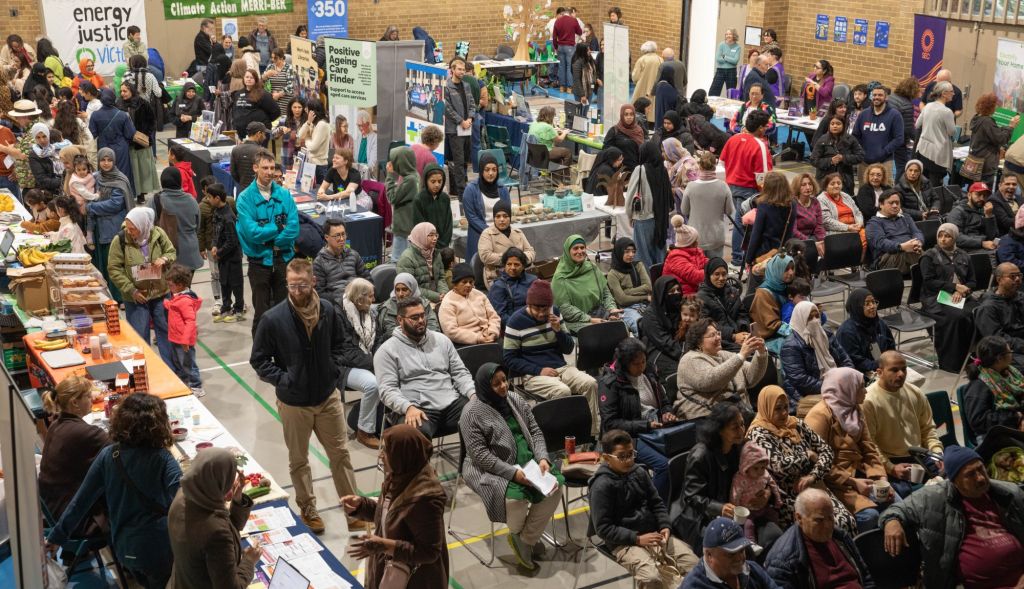Large room full on people with some sitting looking at a stage and others talking to stallholders.