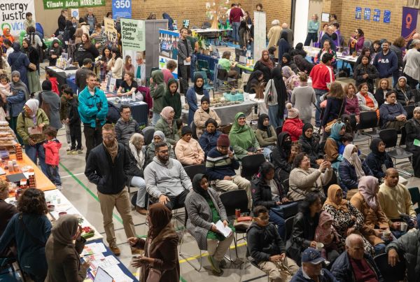 Large room full on people with some sitting looking at a stage and others talking to stallholders.