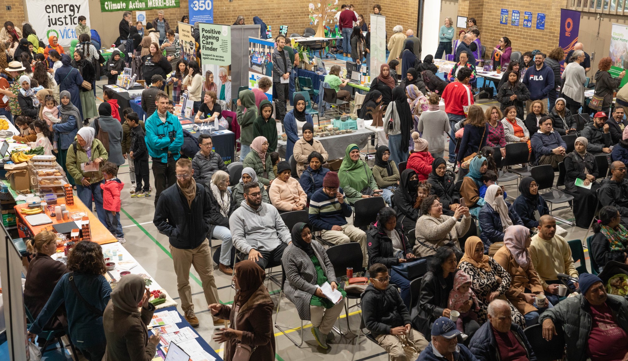 Large room full on people with some sitting looking at a stage and others talking to stallholders.