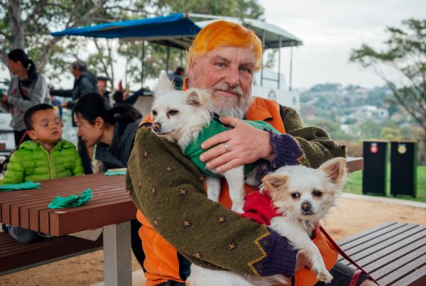 Man with orange hair sitting on a park bench with two little dogs