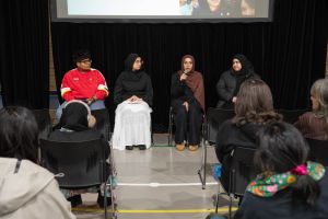 Four young people sitting in front of screen and talking into microphone