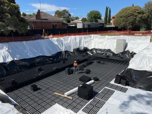 A bog whole in ground which is lined with white sheeting and black plastic moulds to make a tank. Person standing in middle.