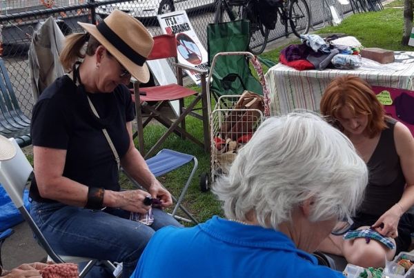 Three women sitting around in a park mending clothes