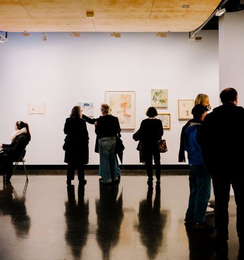 Six people standing in a gallery space looking at artworks on the wall