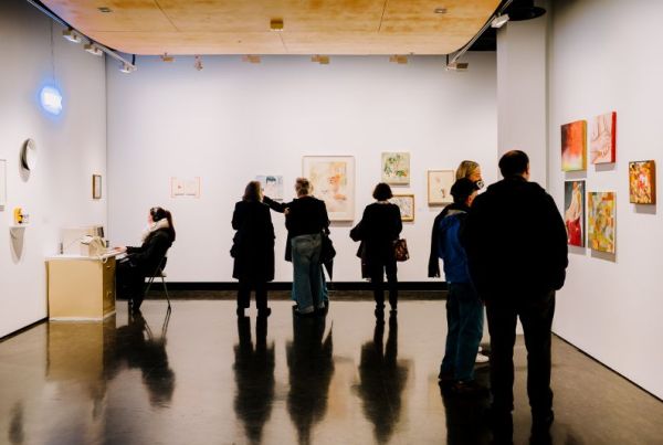 Six people standing in a gallery space looking at artworks on the wall