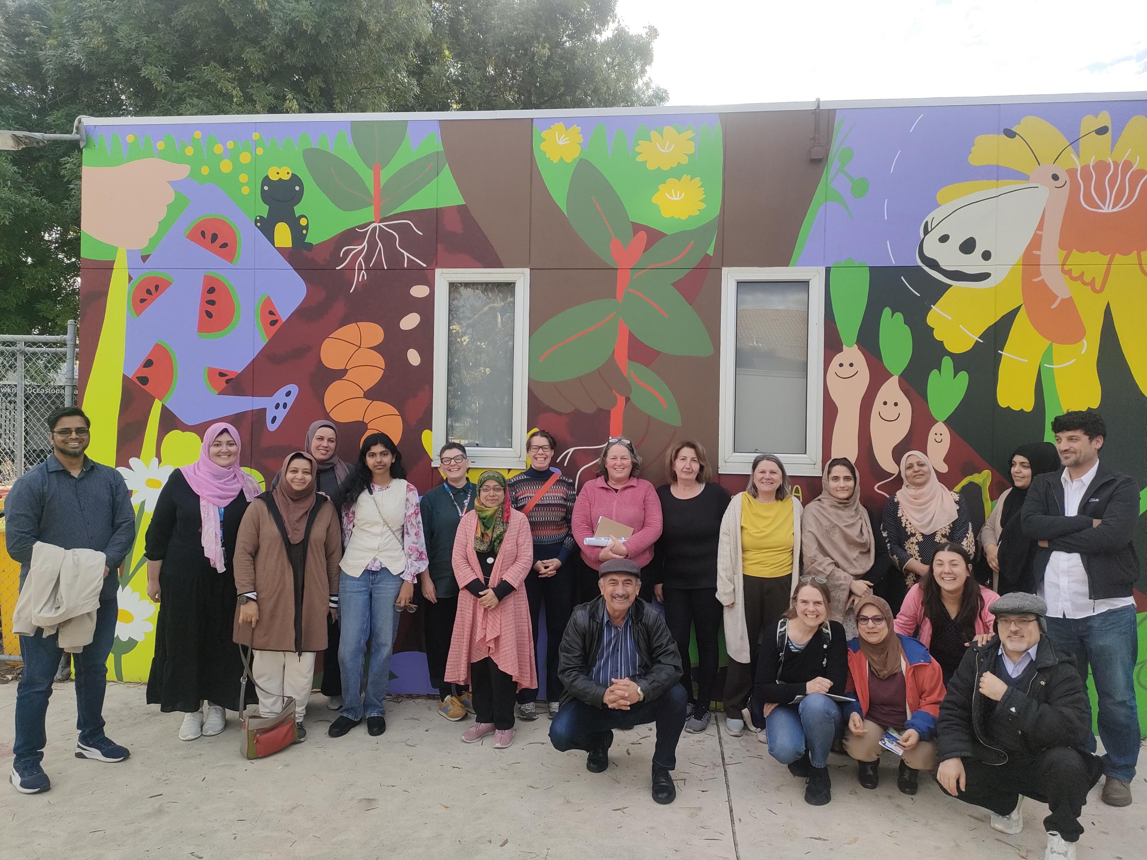 A group of people from diverse backgrounds in standing in front of a colourful mural