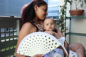 Women with a baby on he rlap looking hot and trying to cool down with a fan