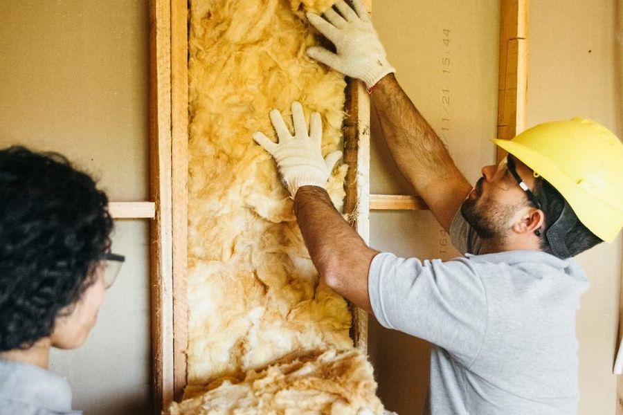 Tradesperson in a yellow hard-hat installing wall insulation