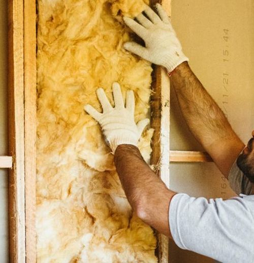 Tradesperson in a yellow hard-hat installing wall insulation