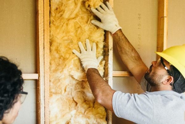 Tradesperson in a yellow hard-hat installing wall insulation