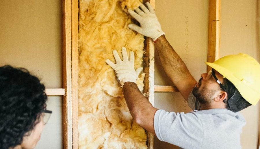 Tradesperson in a yellow hard-hat installing wall insulation