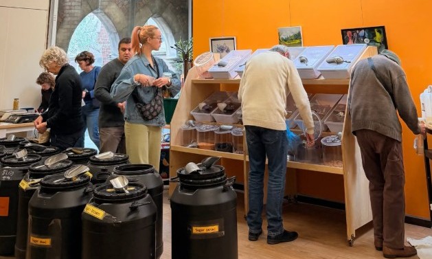 Photo with drums full of food in foreground and people walking into a room and scooping food into containers