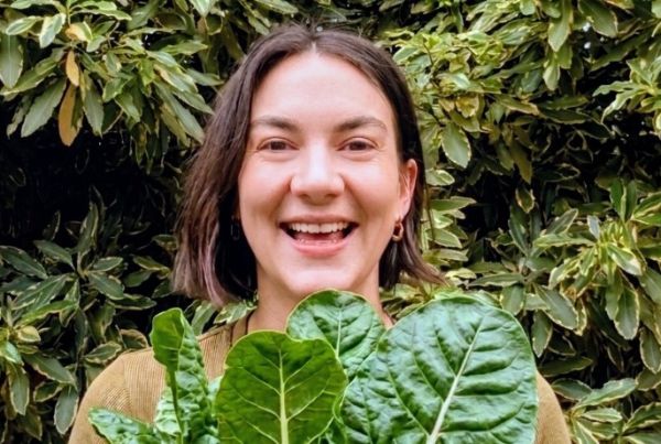 Photo of women smiling and holding a bunch of silverbeet with garden in background
