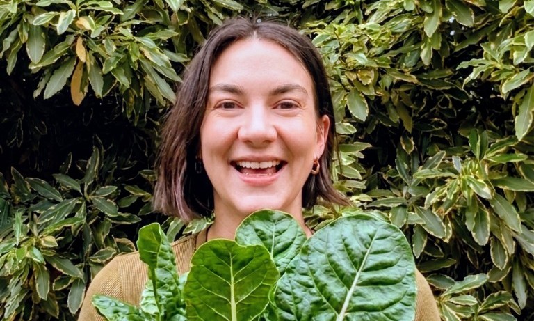 Photo of women smiling and holding a bunch of silverbeet with garden in background