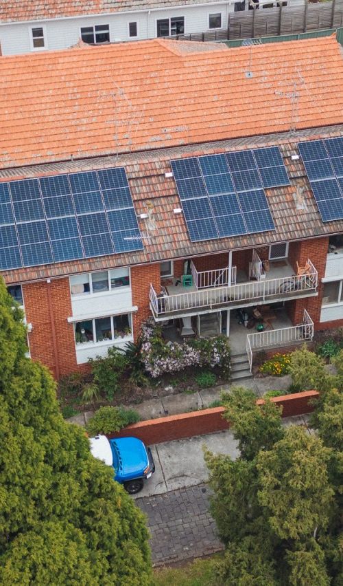 Ariel photo of a three-storey brick apartment with solar on its roof and trees in foreground
