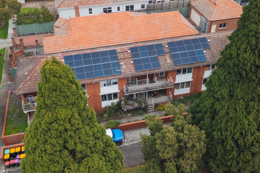 Ariel photo of a three-storey brick apartment with solar on its roof and trees in foreground