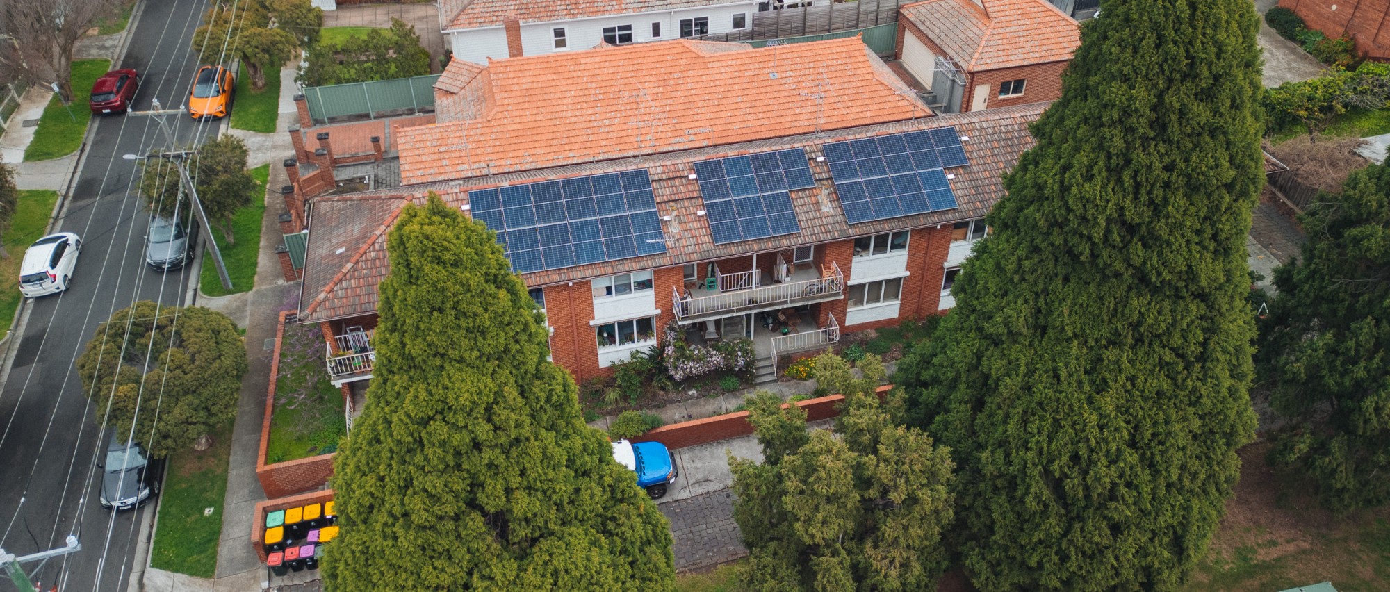 Ariel photo of a three-storey brick apartment with solar on its roof and trees in foreground