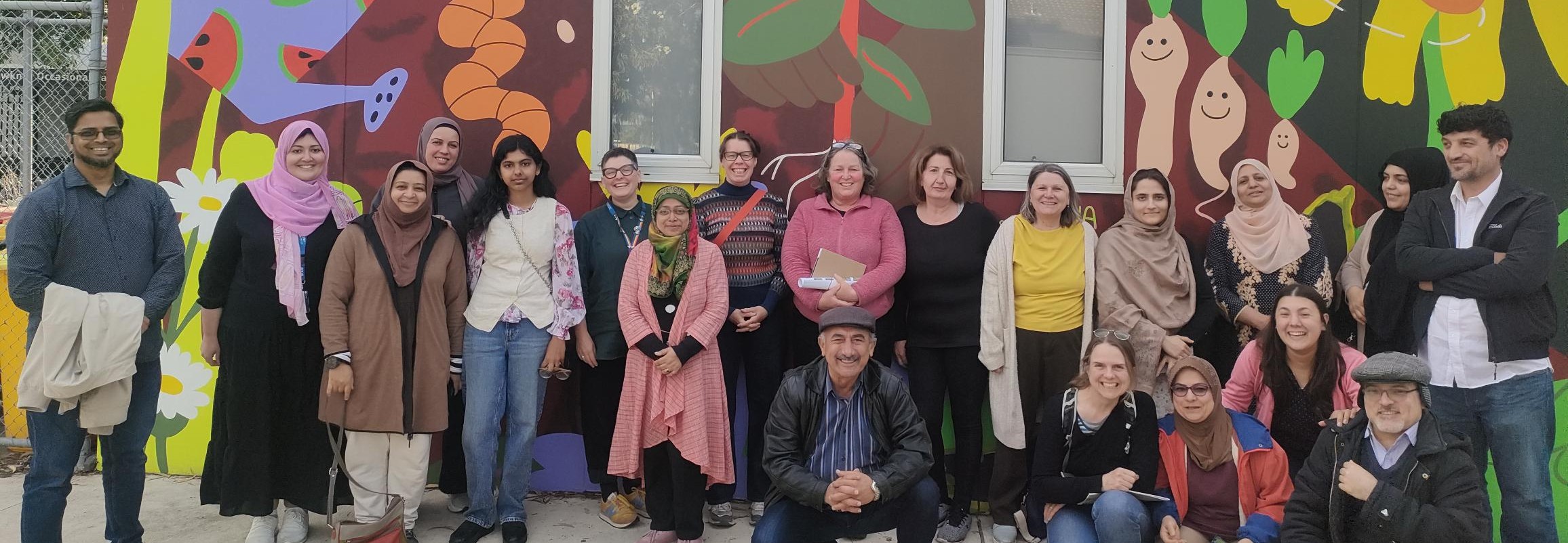 Group of people of diverse ages and cultures standing in front on a coloufull mural